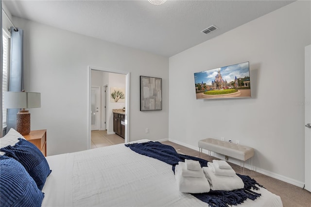 bedroom with light carpet, a textured ceiling, and ensuite bathroom