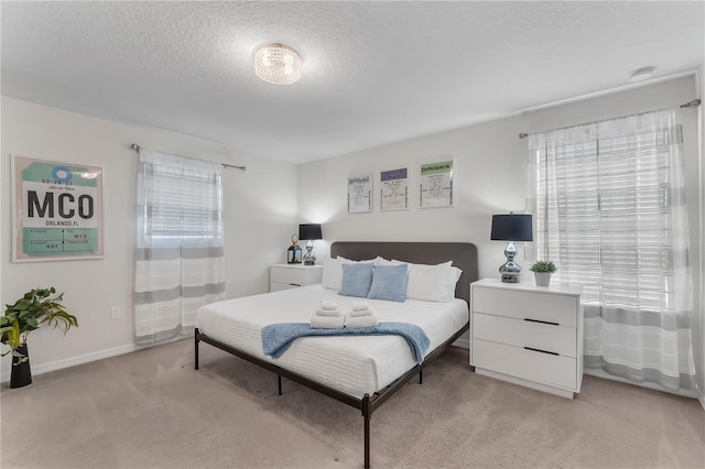 bedroom with light colored carpet, a textured ceiling, and multiple windows