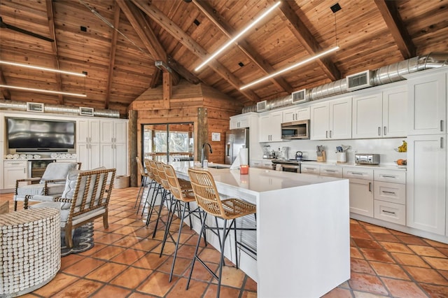 kitchen featuring a kitchen bar, appliances with stainless steel finishes, a kitchen island with sink, white cabinetry, and wood walls