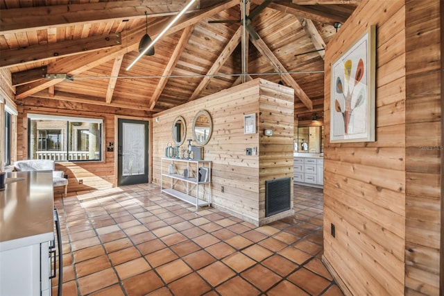 interior space featuring tile patterned floors, lofted ceiling with beams, wooden ceiling, white cabinets, and wood walls