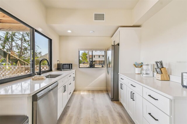 kitchen with kitchen peninsula, appliances with stainless steel finishes, sink, light hardwood / wood-style flooring, and white cabinetry