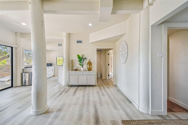 corridor with light wood-type flooring and ornate columns