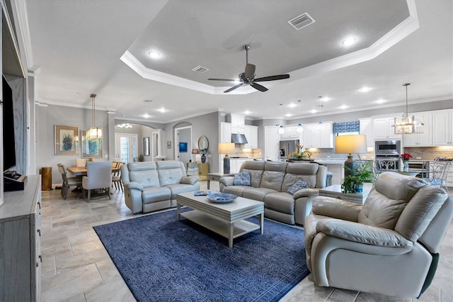 living room with ceiling fan with notable chandelier, a raised ceiling, and crown molding