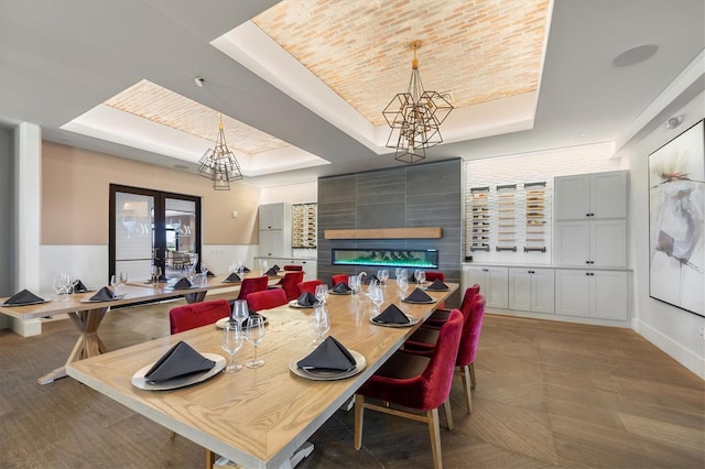 dining space featuring a notable chandelier, a large fireplace, a raised ceiling, and french doors