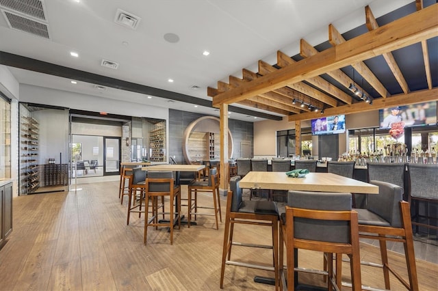 dining room featuring bar area, beamed ceiling, and light wood-type flooring