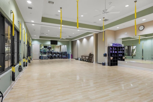 exercise room with light wood-type flooring, a tray ceiling, ceiling fan, and crown molding