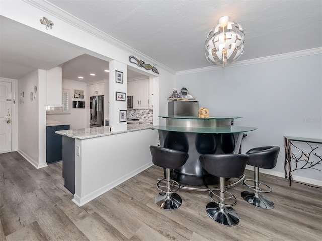 kitchen featuring white cabinetry, light stone counters, stainless steel refrigerator with ice dispenser, kitchen peninsula, and decorative backsplash