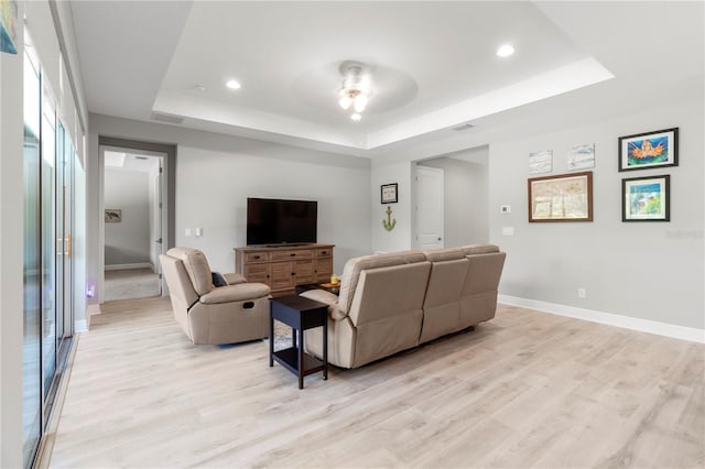 living room with ceiling fan, a raised ceiling, and light wood-type flooring