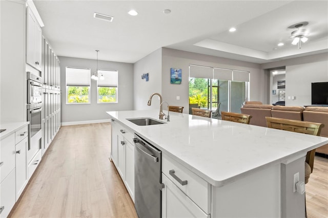 kitchen with light stone countertops, appliances with stainless steel finishes, sink, white cabinets, and an island with sink