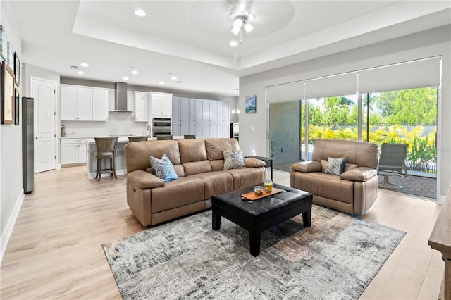 living room with ceiling fan, light hardwood / wood-style floors, and a tray ceiling