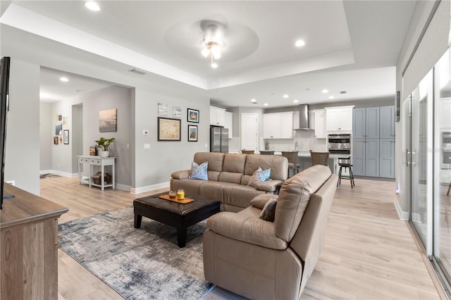 living room with light wood-type flooring, a tray ceiling, and ceiling fan