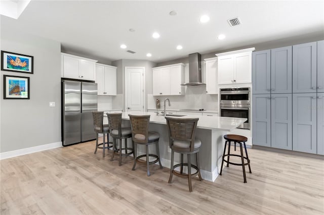 kitchen with a kitchen island with sink, white cabinets, wall chimney exhaust hood, appliances with stainless steel finishes, and a breakfast bar area