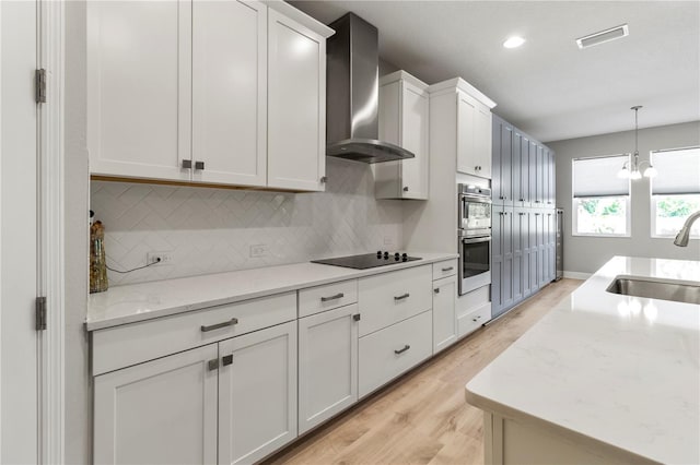 kitchen with light stone countertops, sink, wall chimney exhaust hood, light hardwood / wood-style floors, and white cabinets