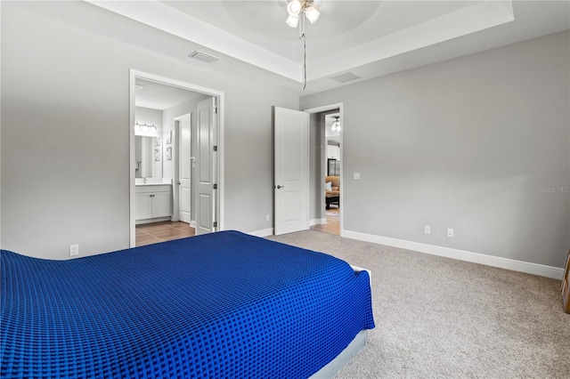 unfurnished bedroom with light colored carpet, ceiling fan, a tray ceiling, and ensuite bathroom