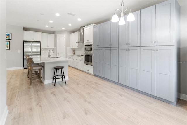 kitchen with appliances with stainless steel finishes, wall chimney range hood, a center island with sink, hanging light fixtures, and a breakfast bar area