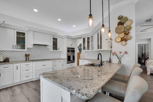 kitchen with a kitchen breakfast bar, double oven, sink, pendant lighting, and white cabinetry