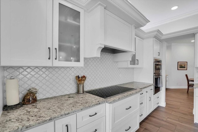 kitchen with black electric stovetop, white cabinets, light hardwood / wood-style flooring, ornamental molding, and light stone counters