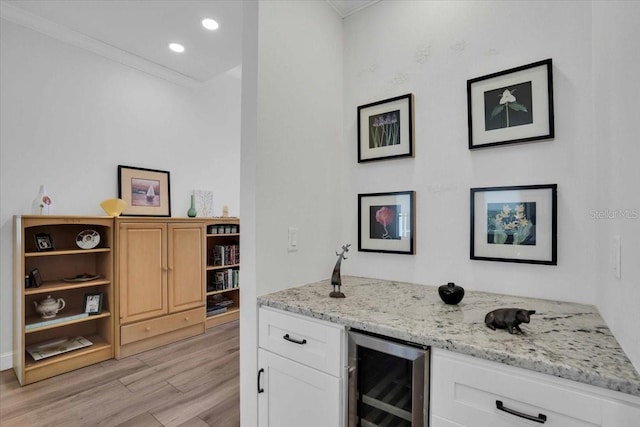 bar featuring light stone countertops, beverage cooler, light hardwood / wood-style floors, white cabinets, and ornamental molding