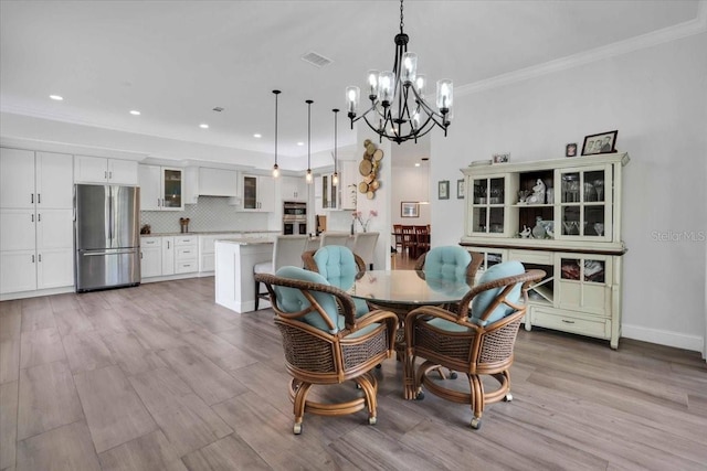 dining space featuring light wood-type flooring, ornamental molding, and an inviting chandelier