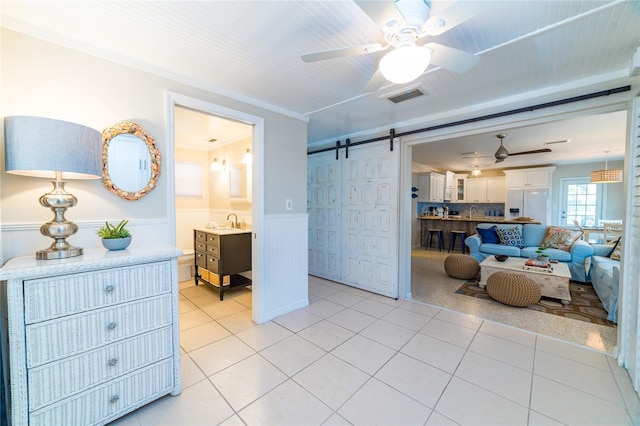 bedroom with sink, a barn door, white refrigerator with ice dispenser, crown molding, and light tile patterned floors