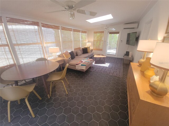 living area with a skylight, dark tile patterned floors, a ceiling fan, and a wall mounted AC