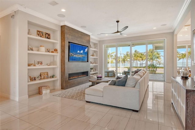 living room featuring built in shelves, ceiling fan, light tile patterned floors, ornamental molding, and a large fireplace