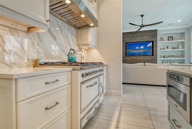 kitchen with gas stove, ceiling fan, light tile patterned floors, white cabinets, and range hood