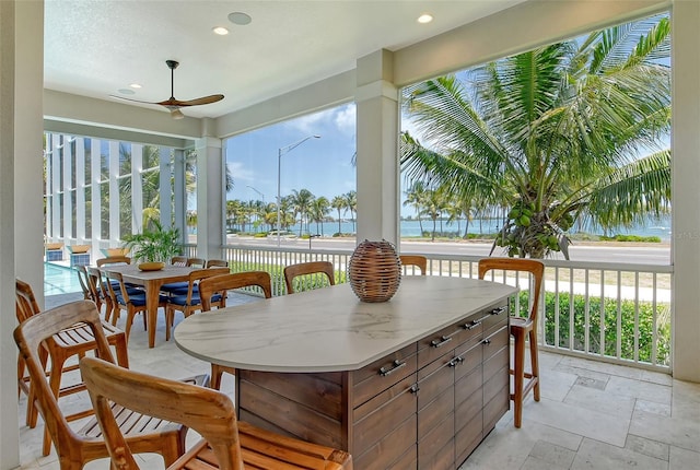 sunroom with ceiling fan and a water view