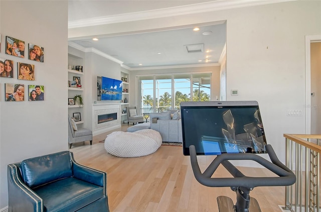 living area featuring built in shelves, crown molding, and wood-type flooring