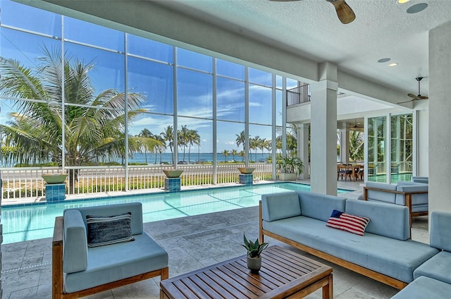 view of swimming pool with ceiling fan, a water view, an outdoor living space, and a patio