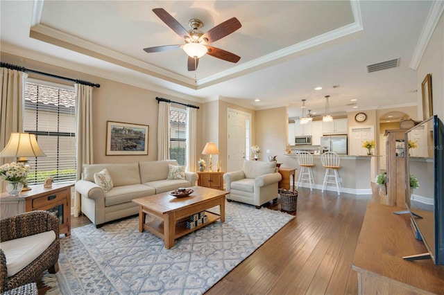 living room featuring light wood-type flooring, a raised ceiling, and crown molding