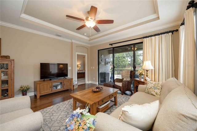 living room with hardwood / wood-style flooring, ceiling fan, ornamental molding, and a tray ceiling