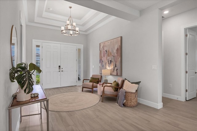 entrance foyer featuring a chandelier, a raised ceiling, ornamental molding, and light hardwood / wood-style flooring