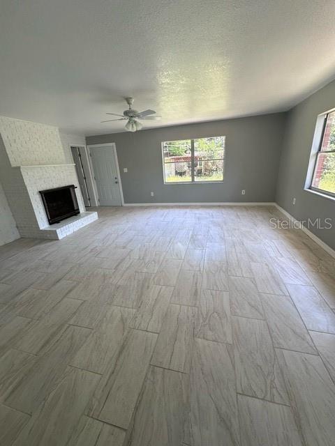 unfurnished living room featuring ceiling fan, a textured ceiling, a wealth of natural light, and a brick fireplace