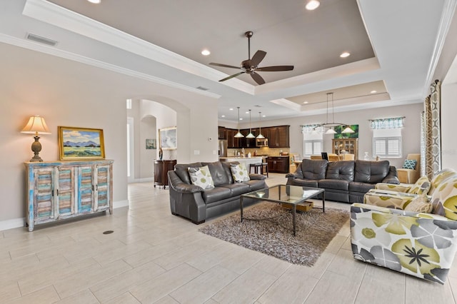 living room with a raised ceiling, ceiling fan, and ornamental molding