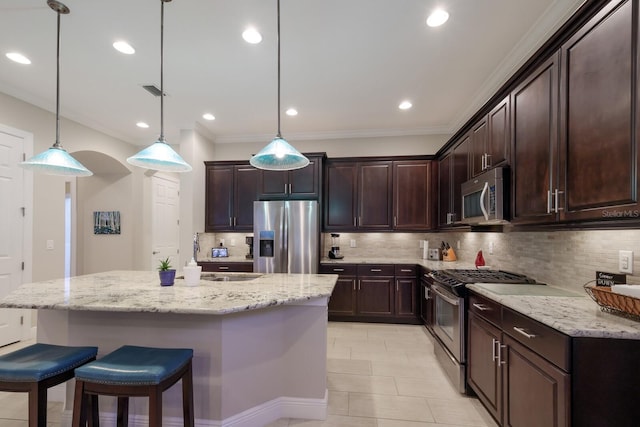 kitchen with dark brown cabinets, a center island with sink, decorative light fixtures, and appliances with stainless steel finishes