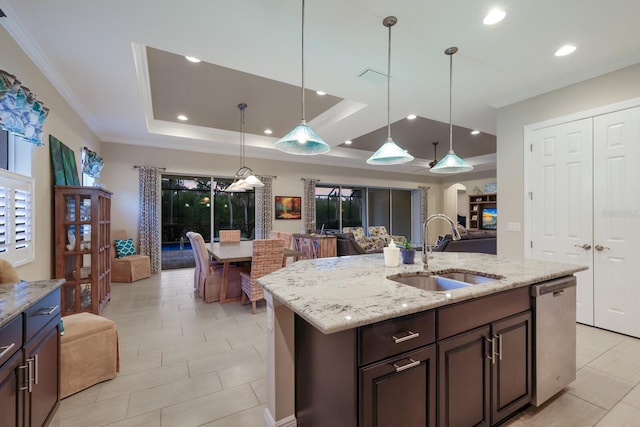 kitchen with dishwasher, a kitchen island with sink, sink, a tray ceiling, and light stone counters