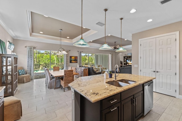 kitchen with dishwasher, sink, a raised ceiling, light stone counters, and an island with sink