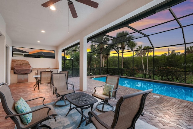 pool at dusk featuring a lanai, an outdoor kitchen, ceiling fan, and a patio area