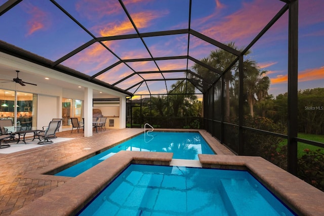 pool at dusk featuring an in ground hot tub, a patio area, ceiling fan, and a lanai