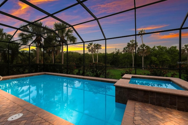 pool at dusk featuring a lanai and an in ground hot tub