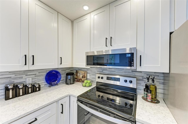 kitchen featuring white cabinets, decorative backsplash, light stone counters, and appliances with stainless steel finishes