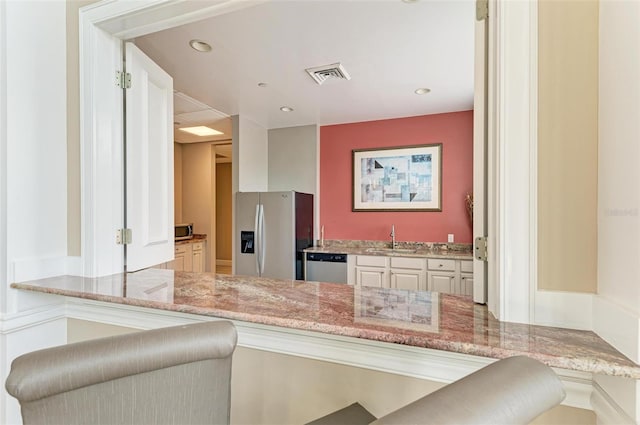 kitchen featuring a kitchen breakfast bar, sink, appliances with stainless steel finishes, light stone counters, and white cabinetry