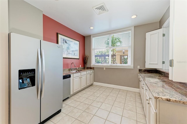 kitchen featuring sink, light tile patterned floors, refrigerator with ice dispenser, stainless steel dishwasher, and white cabinets