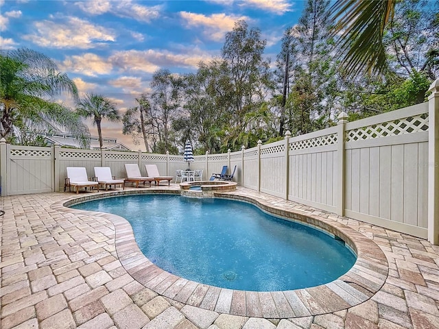 pool at dusk featuring an in ground hot tub and a patio