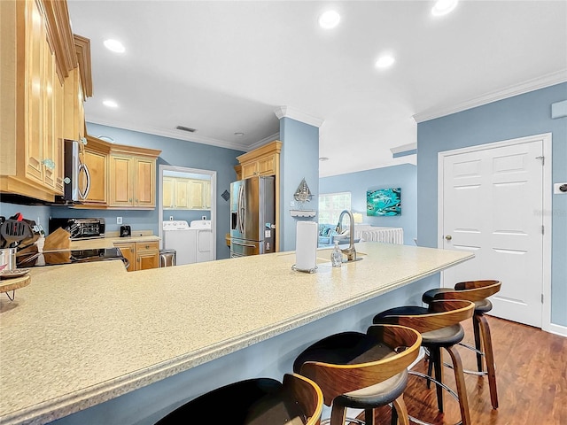 kitchen featuring dark wood-type flooring, separate washer and dryer, appliances with stainless steel finishes, a kitchen breakfast bar, and kitchen peninsula