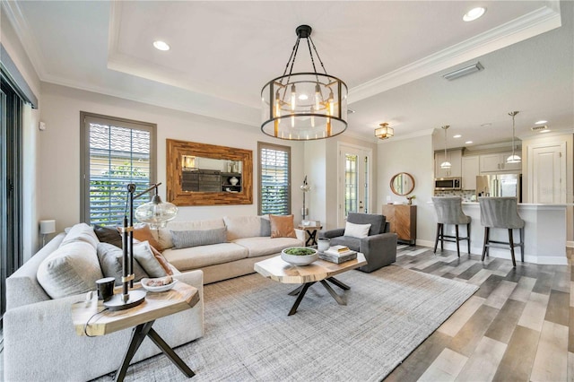 living room with an inviting chandelier, a raised ceiling, light hardwood / wood-style floors, and crown molding