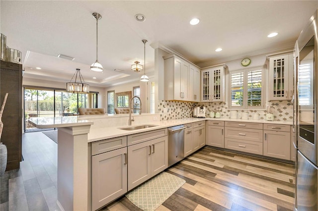 kitchen with sink, stainless steel dishwasher, kitchen peninsula, pendant lighting, and a tray ceiling