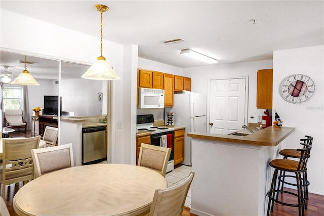 kitchen featuring light hardwood / wood-style flooring, kitchen peninsula, a kitchen breakfast bar, white appliances, and pendant lighting