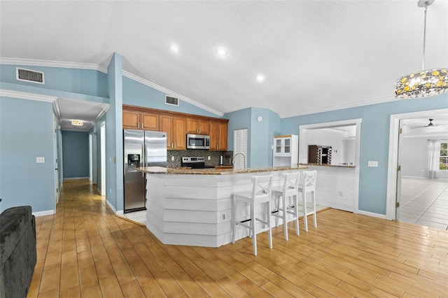 kitchen featuring decorative backsplash, appliances with stainless steel finishes, a kitchen breakfast bar, pendant lighting, and lofted ceiling